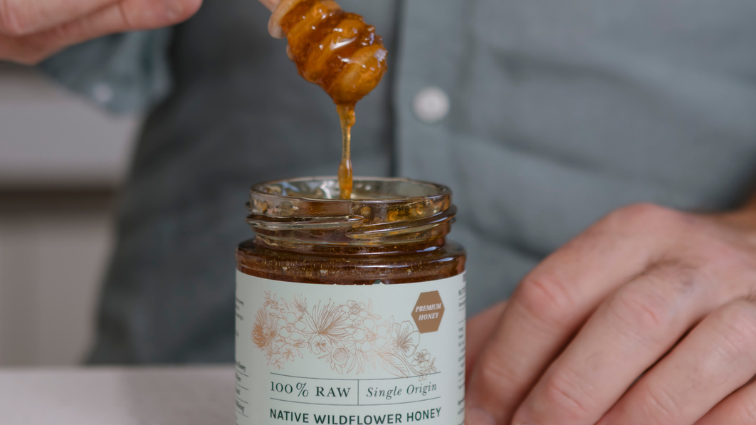 Raw Tasmanian honey drizzling from a wooden dipper into a jar of native wildflower honey